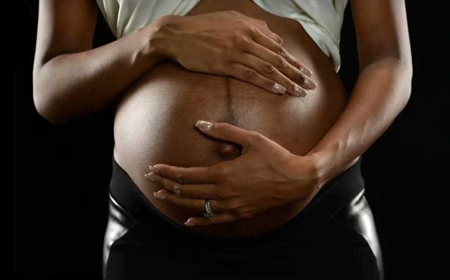 Pregnant woman of color holding her belly.